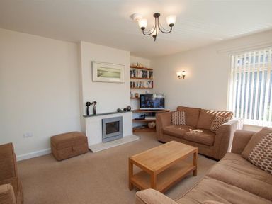 A living room with brown sofas a wooden coffee table a fireplace and a television at Bield How in Ambleside