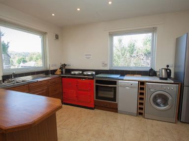 A kitchen with a wooden countertop a red stove oven dishwasher washing machine and two windows at Bield How in Ambleside