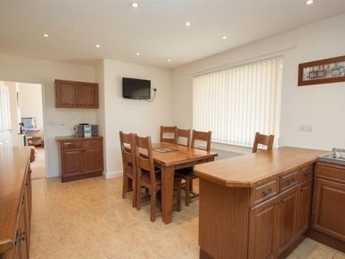 A kitchen with wooden cabinets a dining table with six chairs and a wall mounted television at Bield How in Ambleside