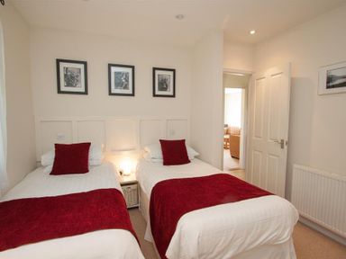 A bedroom with two single beds with red throws and pillows three framed pictures on the wall at Bield How in Ambleside