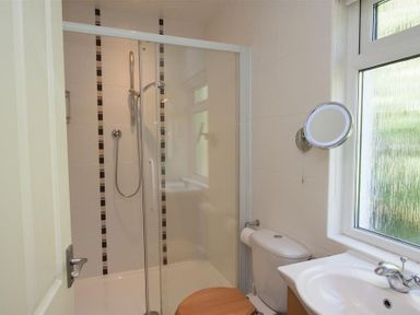 A bathroom with a shower enclosure a toilet a sink and a wall-mounted mirror at Bield How in Ambleside