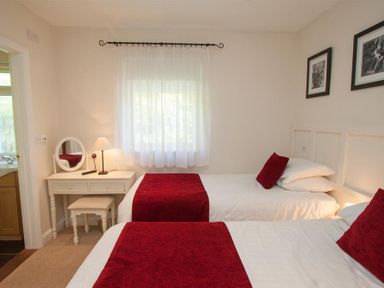 A bedroom with two single beds red runners red cushions a white dressing table with a mirror and lamp at Bield How in Ambleside
