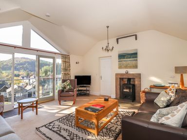 A living room with a sofa an armchair coffee table fireplace and windows showing a hillside view at Garden House in Ambleside