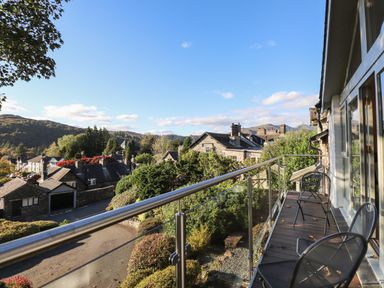 A balcony with metal chairs overlooking a residential area with stone houses and hills at Garden House in Ambleside