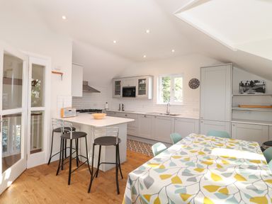 A kitchen with a breakfast bar and stools a dining table with a leaf patterned tablecloth and grey cabinets at Garden House in Ambleside