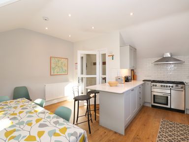 A kitchen and dining area with a table covered with a leaf patterned cloth and chairs and an island with stools at Garden House in Ambleside