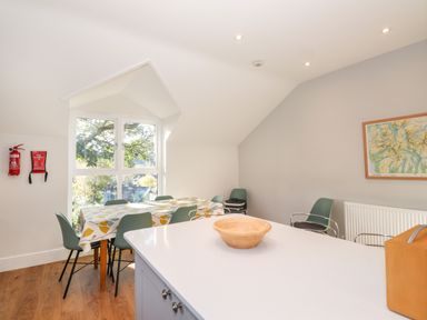 A dining area with a table covered with a patterned tablecloth surrounded by six chairs near a window in Garden House Ambleside