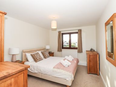 A bedroom with a double bed two bedside tables with lamps a wooden dresser and window with curtains at Garden House in Ambleside