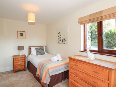 A bedroom with a single bed side table with lamp and a chest of drawers with a window at Garden House Ambleside