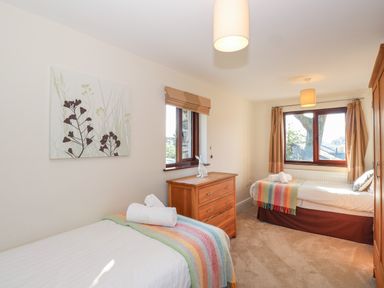 A bedroom with two single beds a wooden chest of drawers and windows showing trees outside at Garden House in Ambleside
