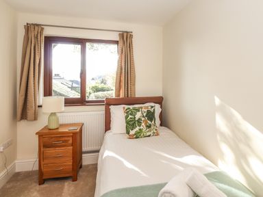 A small bedroom with a single bed a wooden bedside table and a window with curtains at Garden House in Ambleside