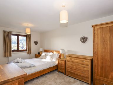 A bedroom with a wooden bed a window with curtains and wooden furniture at Garden House in Ambleside