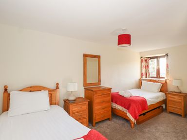 A bedroom with two single beds bedside tables a chest of drawers and a window at Garden House in Ambleside