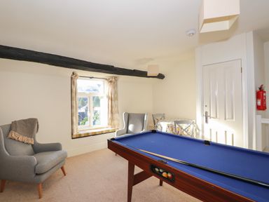 A room with a pool table two armchairs a small table with two chairs and a window seat at Garden House in Ambleside