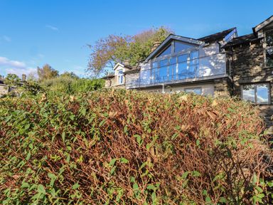 An exterior view of a house with a glass balcony above green shrubs at Garden House in Ambleside
