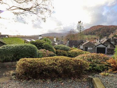 Shrubs and bushes in front of stone houses with hills in the background at Garden House in Ambleside