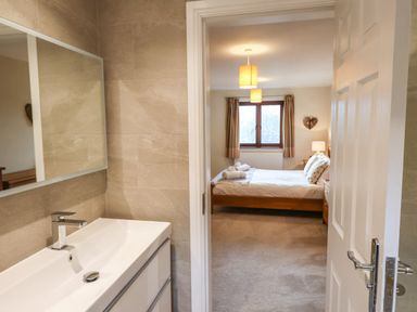 A bathroom sink with mirror and a view into a bedroom with a bed and window at Garden House in Ambleside