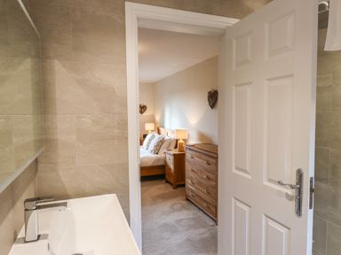A bathroom with a sink and a view into a bedroom with a bed lamps and wooden furniture at Garden House Ambleside