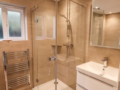 A bathroom with a glass shower enclosure a towel rack a sink and a mirror at Garden House in Ambleside