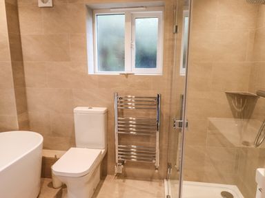 A bathroom with a toilet a bathtub a heated towel rail a window and a glass shower enclosure at Garden House in Ambleside