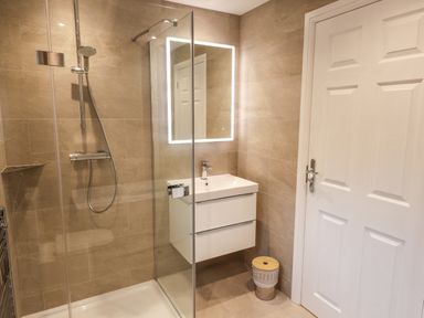 A bathroom with a glass shower enclosure a white sink with drawers a lighted mirror and a closed white door at Garden House in Ambleside