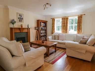 A living room with two beige sofas a wooden coffee table a fireplace and a bookshelf at Orchard House in Ambleside
