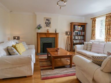 A living room with two white sofas a wooden coffee table a rug a wooden bookshelf and a fireplace at Orchard House Ambleside