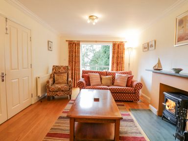 A living room with a red patterned sofa and armchair a wooden coffee table a fireplace and window with orange curtains at Orchard House in Ambleside