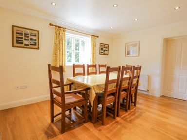 A dining room with a wooden table and eight chairs near a window with yellow curtains at Orchard House in Ambleside