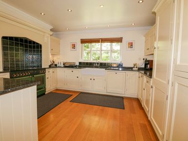 A kitchen with white cabinets black countertops wooden floor and a window at Orchard House Ambleside