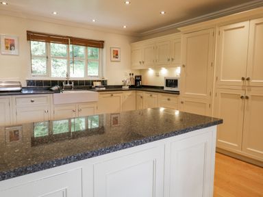 A kitchen with cream cabinets a black countertop an island and a window with wooden blinds at Orchard House in Ambleside
