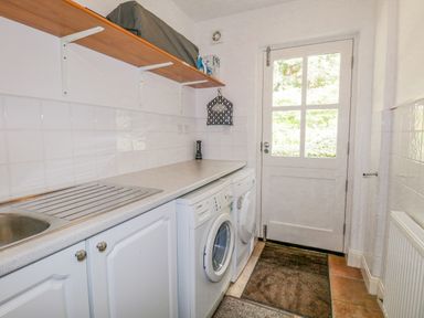 A laundry room with a washing machine and dryer under a countertop and a door with window panels at Orchard House in Ambleside