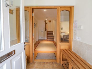 An entrance hallway with a white door wooden bench glass panels and staircase at Orchard House in Ambleside