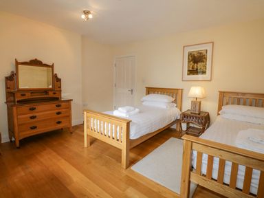 A bedroom with two single wooden beds a wooden dresser with mirror and a nightstand with a lamp at Orchard House in Ambleside