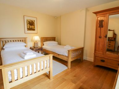 A bedroom with two single wooden beds a bedside table with a lamp a wooden wardrobe and a framed picture on the wall at Orchard House in Ambleside