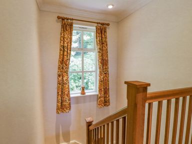 A stairway with wooden railing next to a window with patterned curtains and a ceramic vase on the windowsill at Orchard House in Ambleside