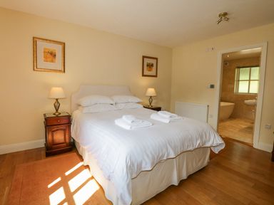A bedroom with a double bed with white linens two bedside tables with lamps two framed pictures on the wall and an en suite bathroom at Orchard House in Ambleside
