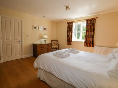 A bedroom with a double bed folded towels on the bed a wooden chest of drawers a chair and window with patterned curtains at Orchard House in Ambleside