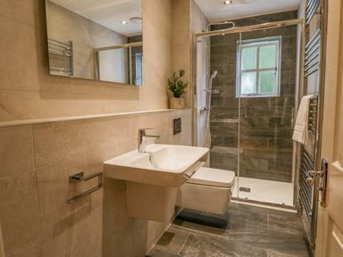A bathroom with a wall-mounted sink and toilet a glass shower enclosure and a window at Orchard House in Ambleside