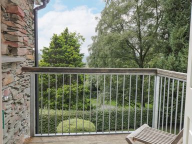 A balcony with metal railings and a wooden chair overlooking trees and bushes at Orchard House in Ambleside