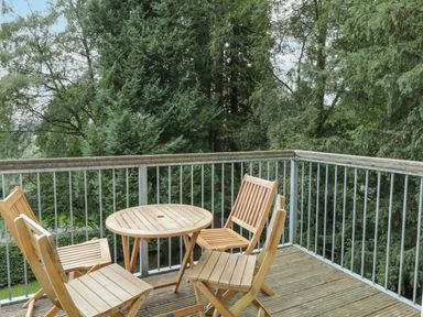 An outdoor balcony with a round wooden table and four wooden chairs surrounded by trees at Orchard House in Ambleside