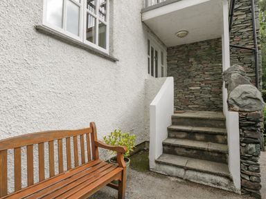 An outdoor area with stone steps leading to a door a wooden bench and a potted plant at Orchard House in Ambleside
