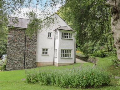 A white house with stone chimney surrounded by trees and garden at Orchard House in Ambleside