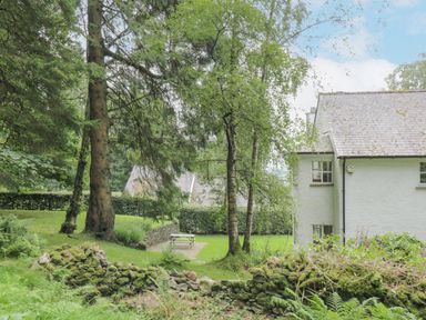 A garden with trees a stone wall a picnic table and part of a white house at Orchard House in Ambleside