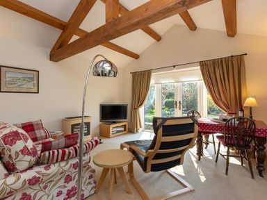 A living room with wooden beams a sofa a TV and a dining table with chairs at Bank Foot in Ambleside