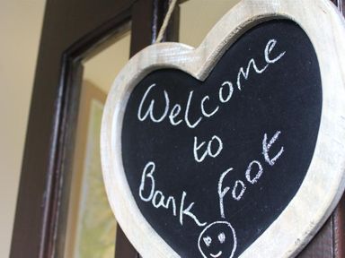 A heart shaped chalkboard sign hanging on a door with welcome to Bank Foot written on it at Bank Foot in Ambleside