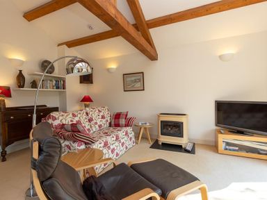 A living room with wooden beams a floral sofa a black leather chair a small fireplace and a television at Bank Foot in Ambleside