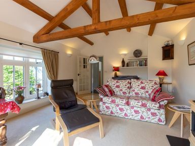 A living room with wooden beams a floral sofa a black armchair and large window at Bank Foot in Ambleside