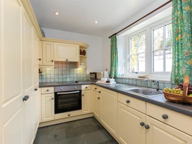A kitchen with cream cabinets a black countertop a sink an oven and green patterned curtains at Bank Foot Ambleside
