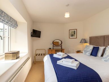 A bedroom with a bed towels on a runner a wall mounted television a dressing table and a window at Bank Foot in Ambleside